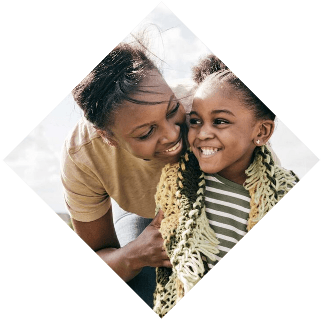 A mother and daughter smile happily as the mother hugs her child.
