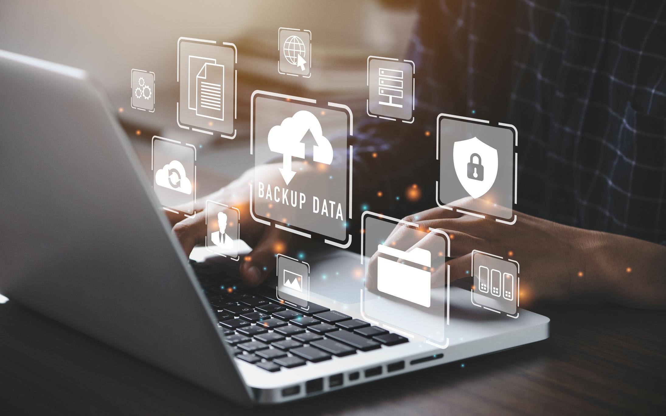 An illustration of data backup in the cloud. It shows a laptop with different icons (such as gears, documents, a cloud upload icon, a lock icon, an image icon and more) floating overtop.