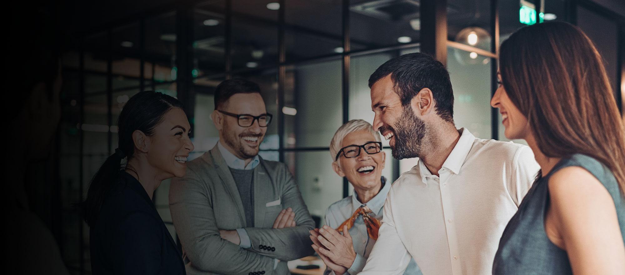 A background image of a group of professional individuals standing and chatting together in an office setting. They are smiling.