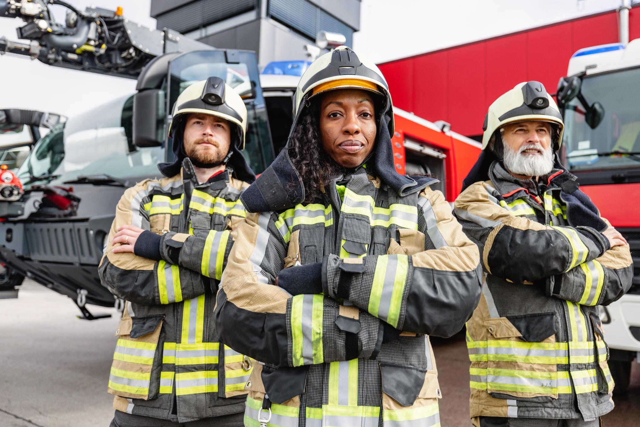 Firefighters wearing fire protective gear, looking at the camera while standing in front of the fire engine.