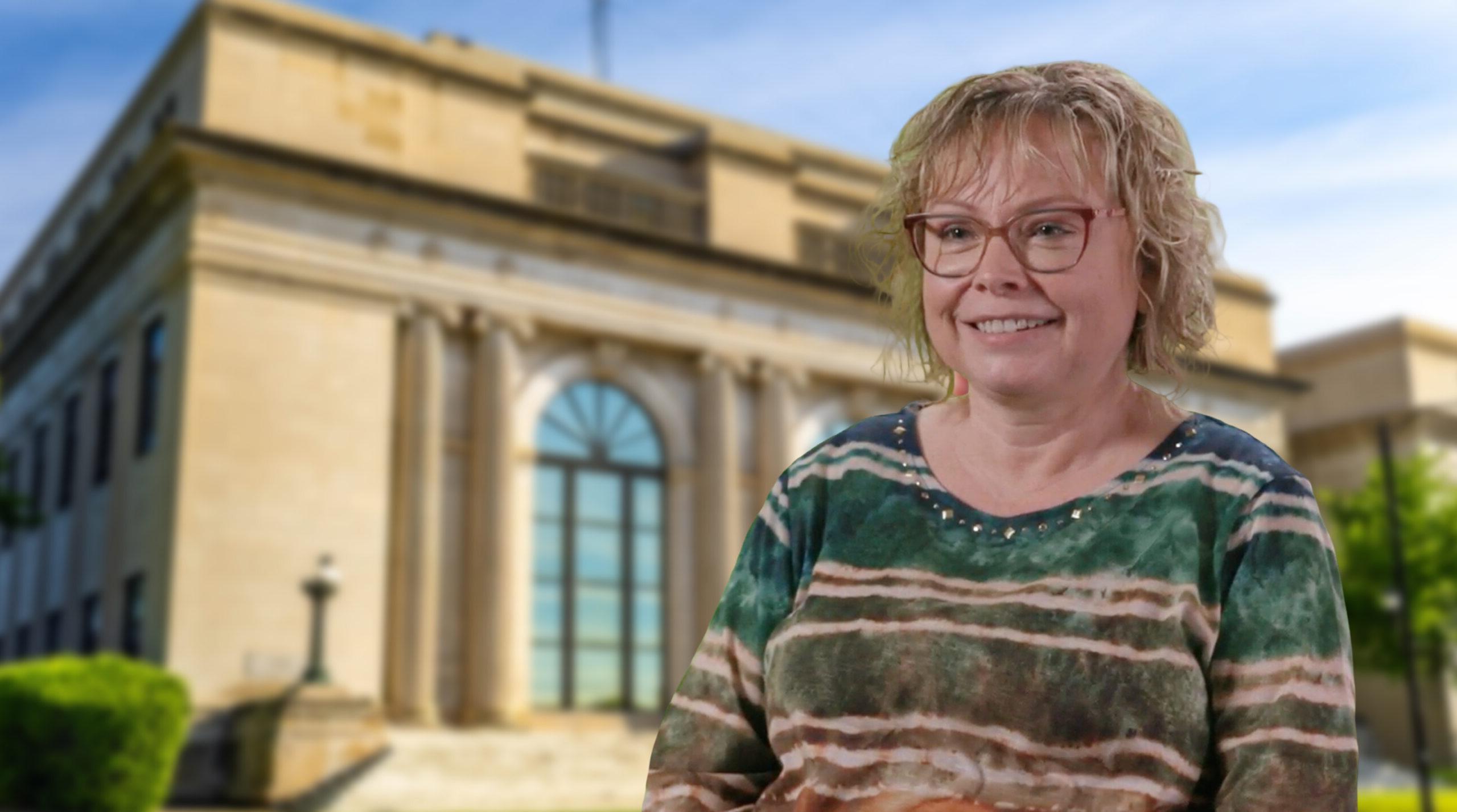 Rhonda Bohn, Computer Tech at Pennington County Sheriff’s Office, smiling in front of a blurred stone government building with an arched window