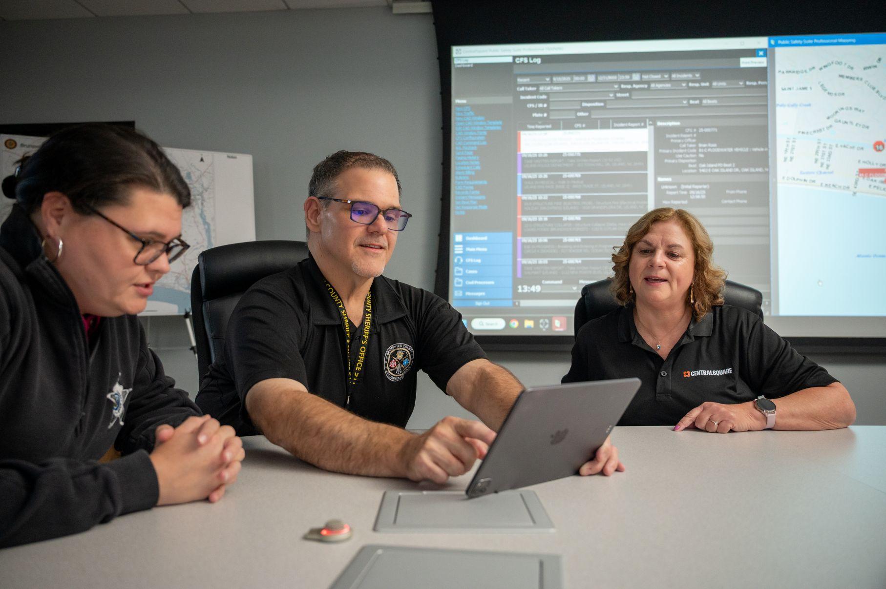 Three people at an office desk looking at a tablet