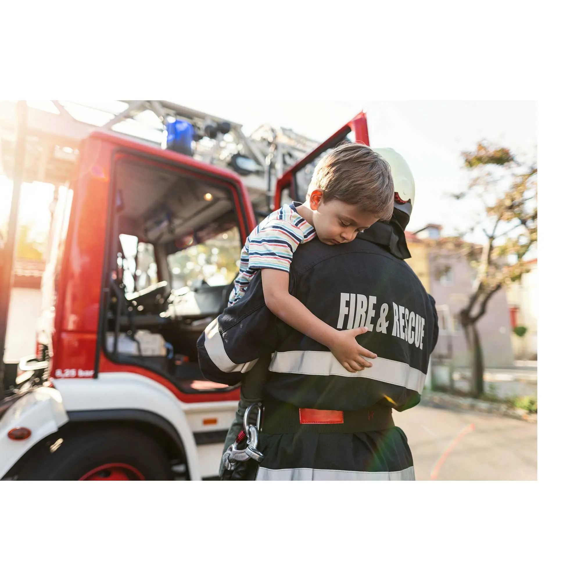 A fire and rescue in full uniform carrying a small child toward a fire truck.