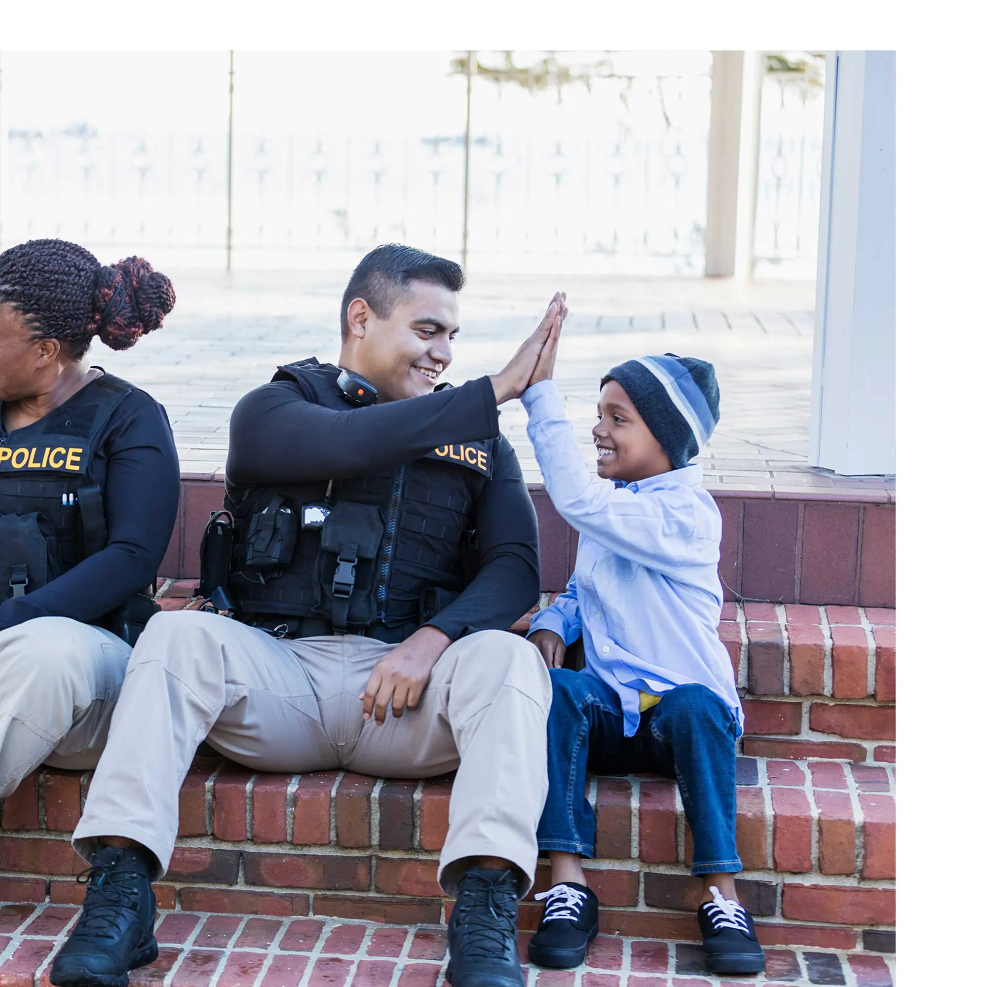A police officer high-fiving a kid in his community on the steps of a building.