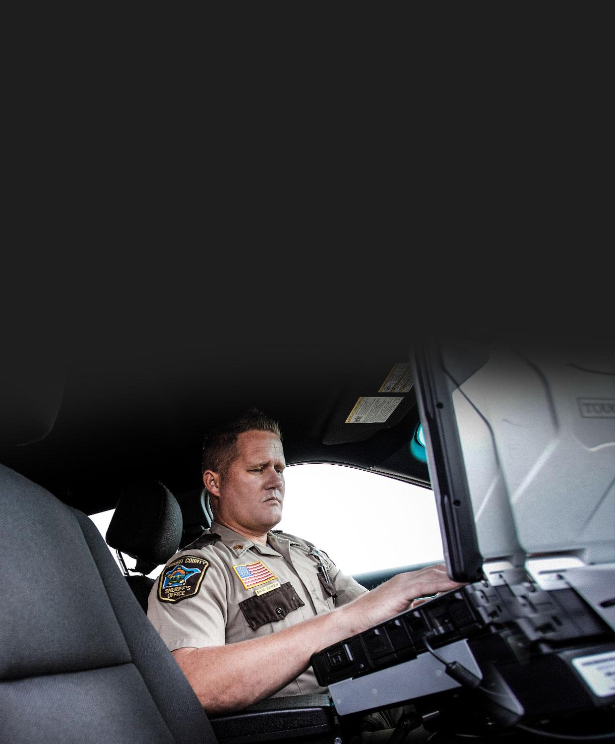 An officer in his squad car using a laptop.